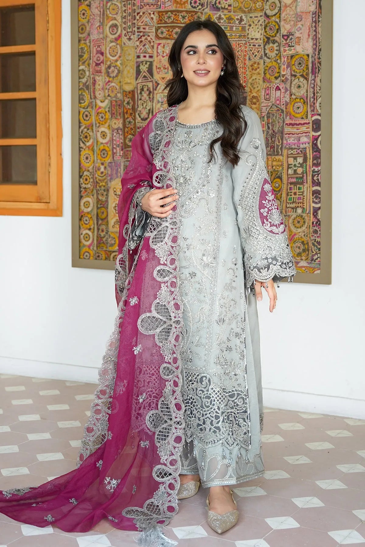 A woman wearing an unstitched 3-piece shirt with embroidery, organza for front and back, and a dupatta in pink with embroidery. Trouser in dyed raw silk with embroidery on the border.