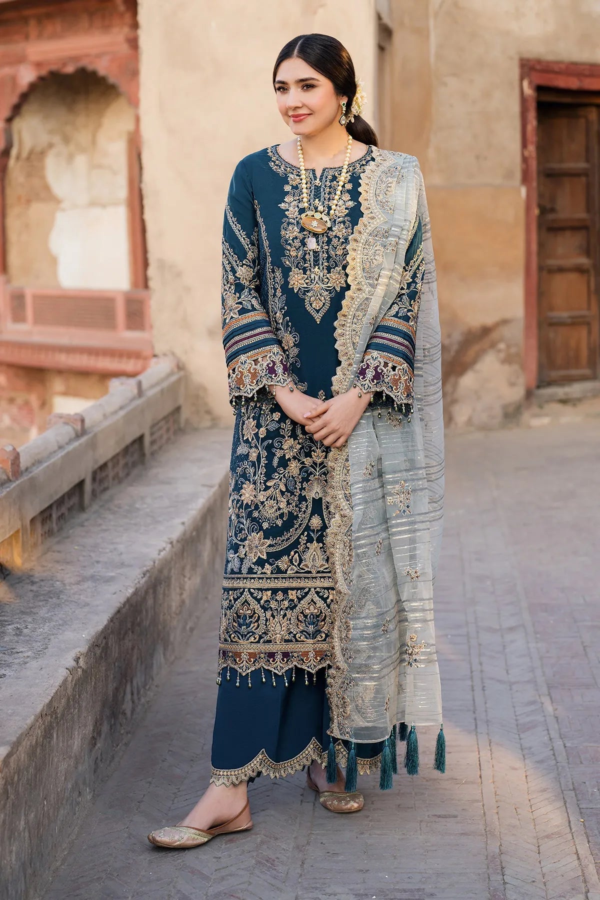 A woman wearing a three-piece teal traditional South Asian outfit with intricate embroidery and an organza dupatta.