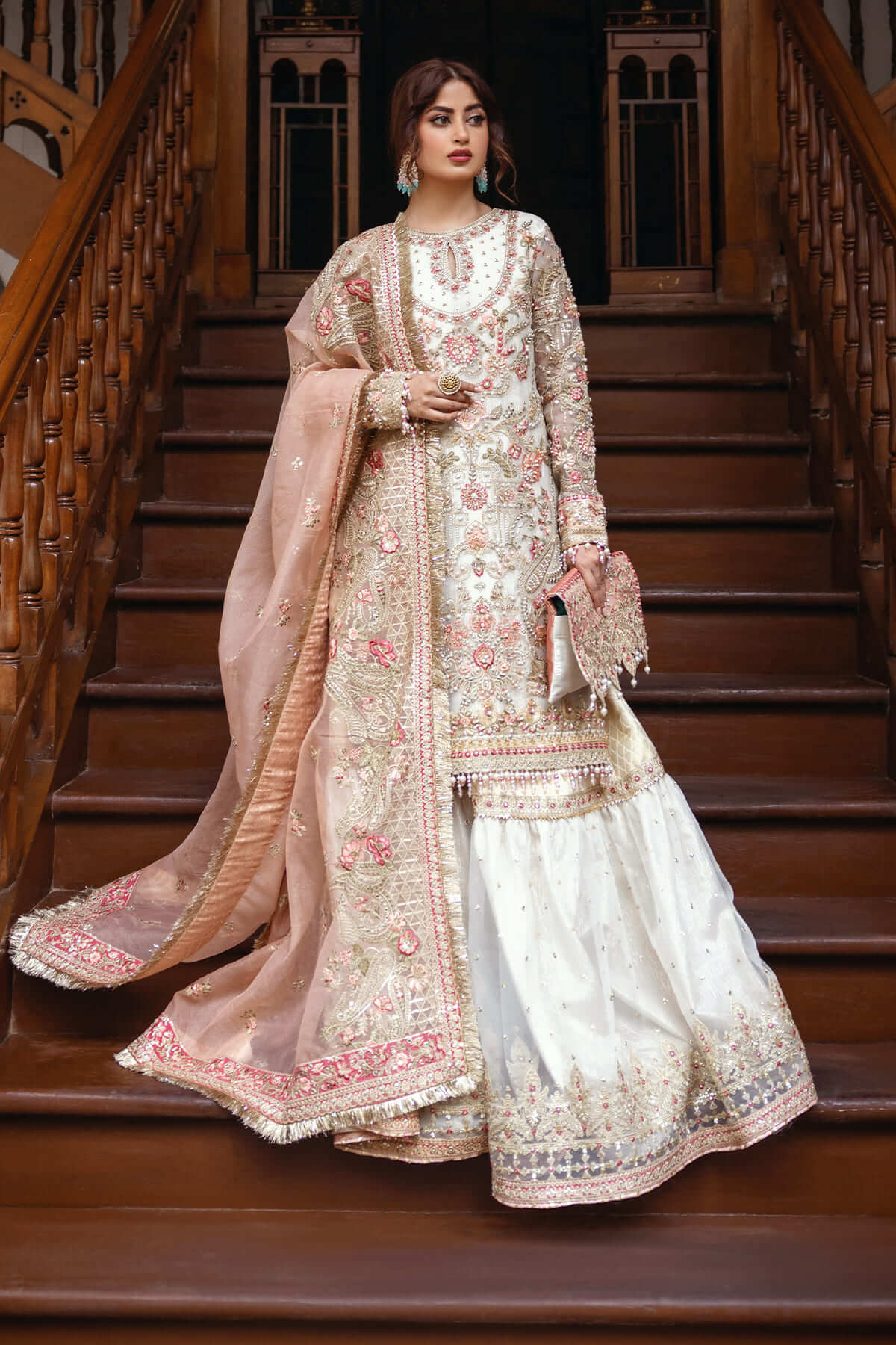A woman wearing a traditional bridal outfit with embroidered organza and katan net fabric, featuring pastel colors and intricate patterns.
