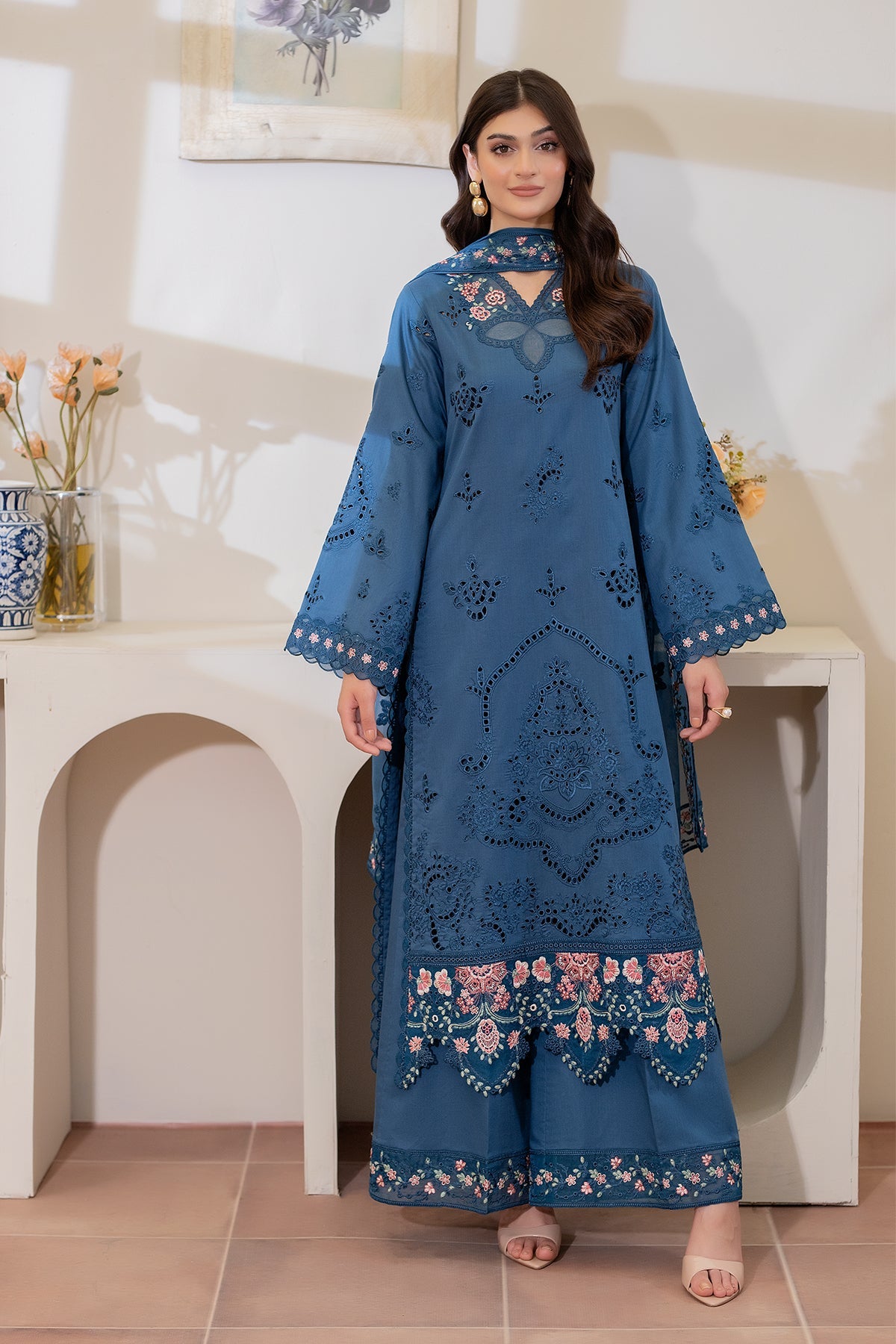 Woman wearing a blue embroidered outfit standing indoors.